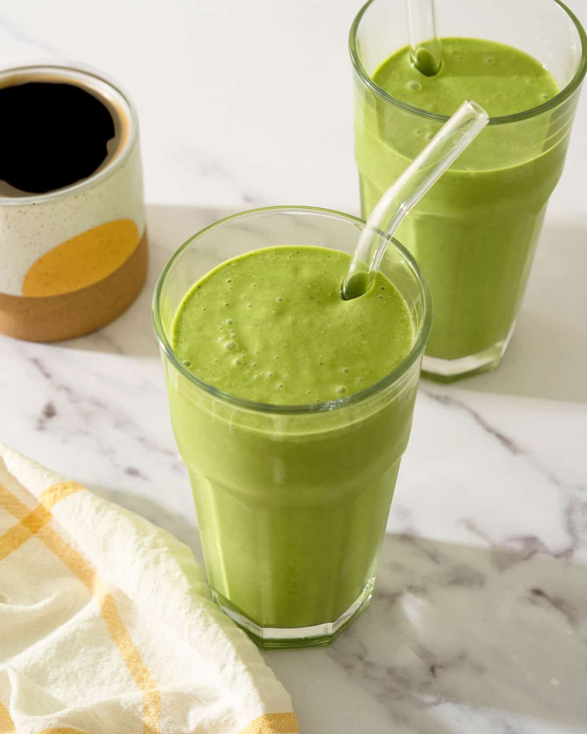 Two kale and spinach smoothies in glasses with straws.