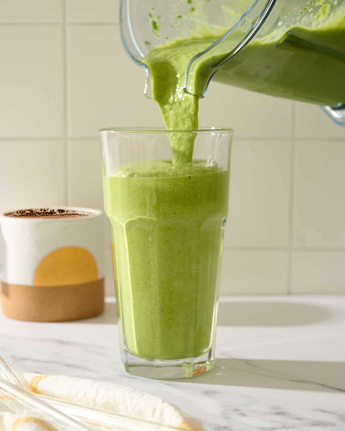 Pouring a green smoothie into glass from a blender pitcher.