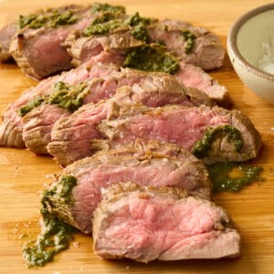 Air fryer carne asada topped with chimichurri on a cutting board.